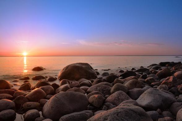 A beautiful pink and blue sky sunset to the horizon at the sea with boulders at the shore