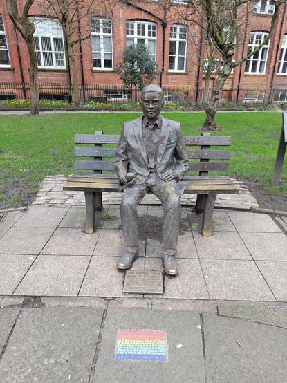 The memorial to Alan Turing sits in Sackville Gardens holding an apple in Manchester. A five-stripe Pride flag mosaic has been added in front.