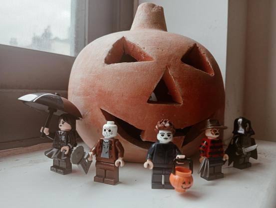 Wednesday Addams, Jason Voorhees, Michael Myers, Freddy Kruger and Ghostface as LEGO minifigures, in front of a clay pumpkin