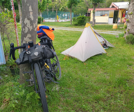 Photo de ma tente tipi installée sur un emplacement de camping. Mon vélo encore adossé contre un arbre.