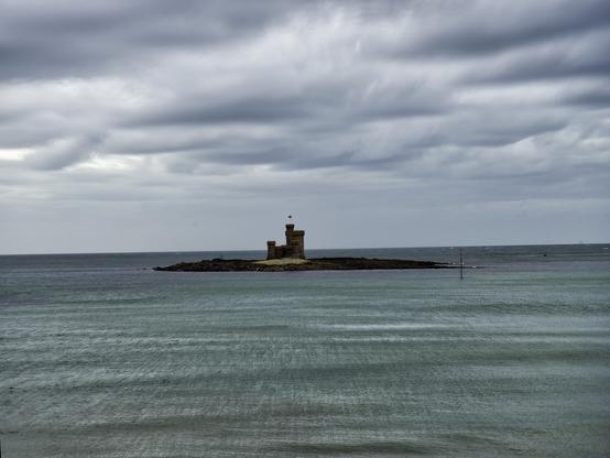a tiny island under heavy grey skies that has a tiny castle built on it