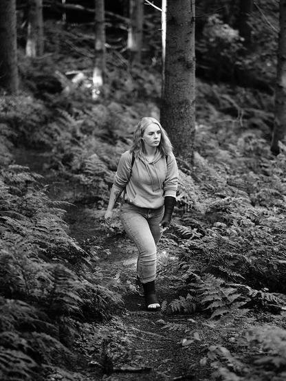 Junge Frau mit Gehgips und Gipsarm auf einer Wanderung durch einen Wald.