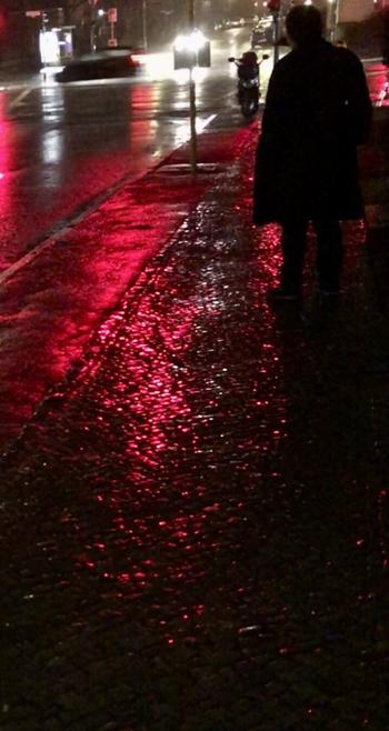 Das Bild zeigt eine nächtliche Straßenszene bei Regen. Im Vordergrund ist ein nasser, gepflasteter Bürgersteig zu sehen, der durch die roten Lichter einer Ampel in rötliches Licht getaucht ist. Im Hintergrund ist eine Person in einem dunklen Mantel zu erkennen, die an einer Kreuzung steht. Im Hintergrund sind auch verschwommene Lichter von Fahrzeugen und Gebäuden erkennbar. Die gesamte Szene ist dunkel und von einer regnerischen Atmosphäre geprägt.

Bereitgestellt von @altbot@fuzzies.wtf, generiert mit Gemini