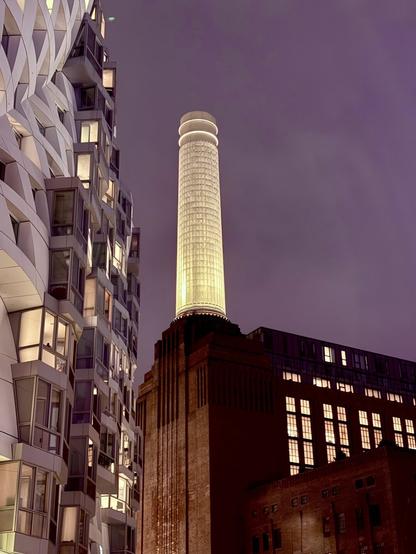 Side view of the Battersea power station at night beneath a purple sky with apartments on the side