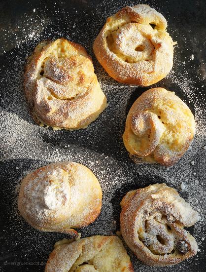 Schwarzer Metalluntergrund. 6 Puddingschnecken mit Puderzucker bestäubt, bepudert...