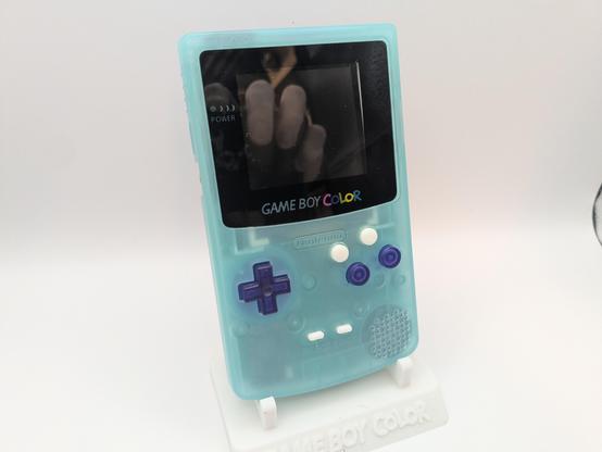 A GBC on a stand, glow in the dark shell with purple buttons and added white X Y buttons above the A and B buttons