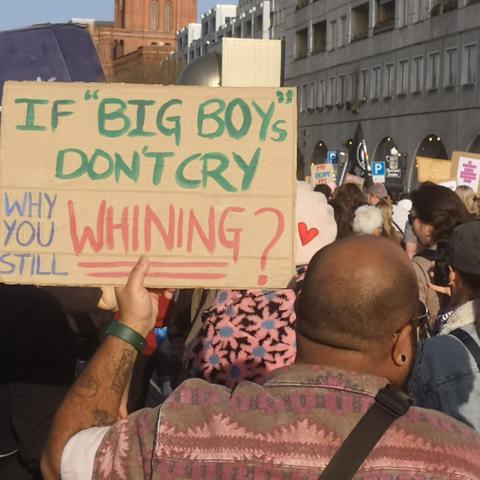 Plakat mit der Frage 'If Big Boys Don't Cry, why you still whining?' auf der 8. März 2025 Demonstration in Berlin. Eine Person im Vordergrund hält das Plakat, während im Hintergrund eine Menschenmenge zu sehen ist.