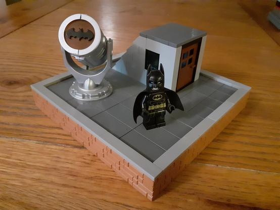 Keaton-Batman standing on a rooftop, next to the Batsignal (in LEGO)