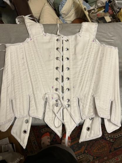 A nearly finished white corset with the lacing in the middle and the straps at the top.