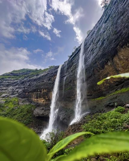White waterfall falling over a cliff into green vegetation and white cloudy sky
