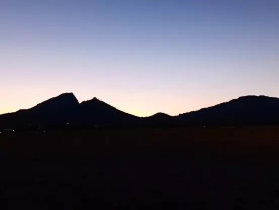 Au crépuscule, une montagne totalement noire se découpe dans un ciel dégagé aux lumières du soleil couchant. On distingue quelques éclairages ici et là dans les parties obscures de la photo.