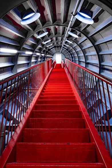 Look-up view on red metallic stairs linking two of the spheres of tha Atomium in Brussels. The Atomium is a Landmark modernist building in Brussels, Belgium, originally constructed as the centrepiece of the 1958 Brussels World's Fair (Expo 58). The Atomium stands 102 metres (335 ft) tall, making it one of the tallest structures in Belgium. Its nine 18-metre-diameter (59 ft) stainless steel clad spheres are connected in the shape of a unit cell that could represent an iron crystal magnified 165 billion times Steel tubes connecting the spheres enclose stairs, escalators and an lift (in the central, vertical tube).