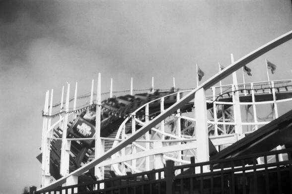 A traditional wooden coaster, with a train swooping around a downward curve.  There is a somewhat dramatic sky behind it.
