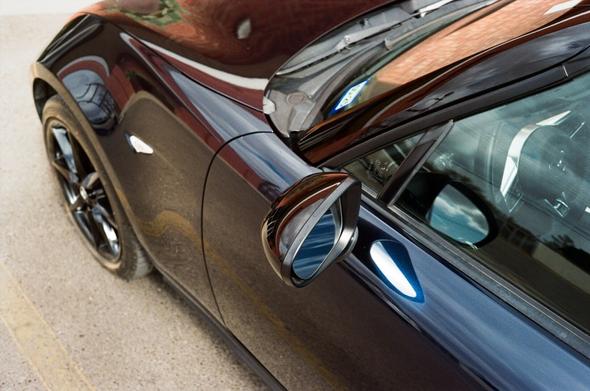 Top down shot at an angle. Looking at the left side mirror of a dark blue Mazda Miata.