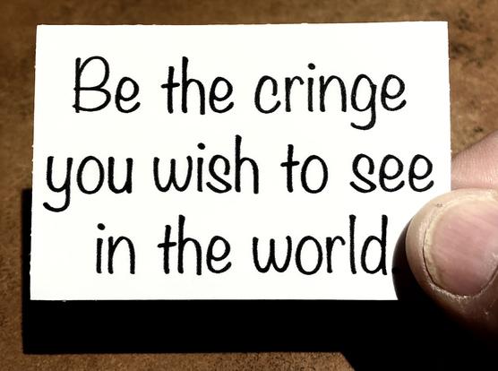 a small black and white sticker being held in my fingers. In a casual style font it says "Be the cringe you wish to see in the world", a riff on the popular (and very cringy) saying "Be the change you wish to see in the world." The sticker is 2" x 3", about the size of a business card.