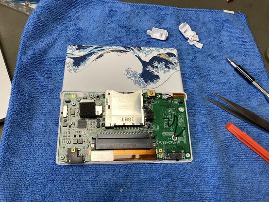 Nintendo DS lite on my workbench with a Hokusai cover showing the famous wave on my workbench. The bottom case is not fitted yet and the circuit board is visible.