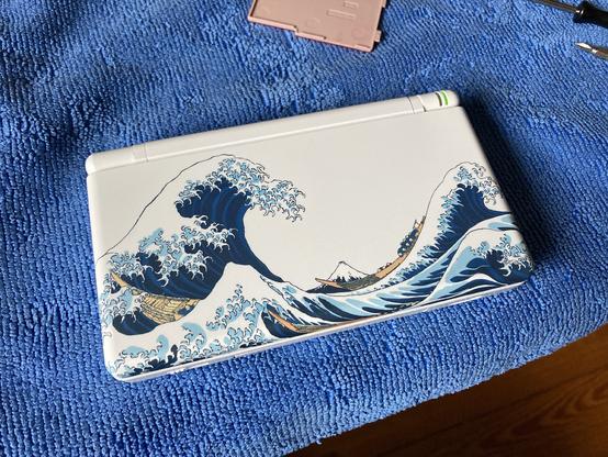 The DS lite with the lid closed, showing the full Hokusai wave graphic.