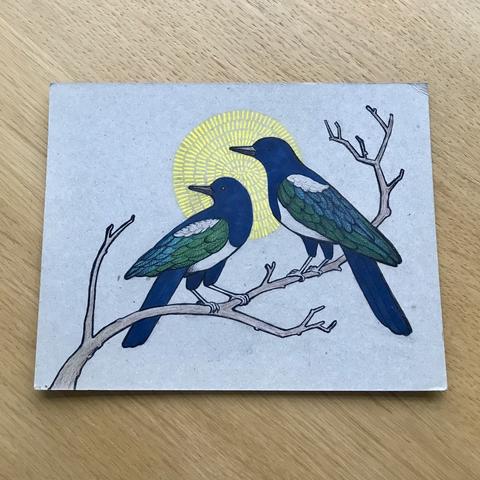 Drawing of two magpies sitting on a branch looking to the left. Behind their heads is a decorative yellow disc.