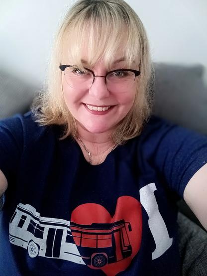 Ich sitze und grinse frontal in die Kamera. Ich trage ein dunkelblaues Shirt. 
Darauf steht 

I ♥️ 🚌