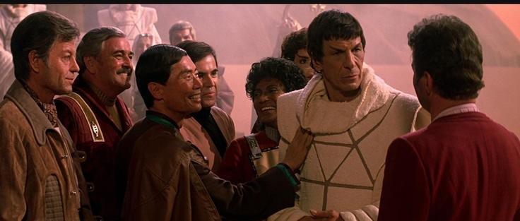 Star Trek The Search for Spock scene. Our Lord and Savior Spock is pictured in a white robe. He stands surrounded by his shipmates who are all older here than they were in the TV show. Sulu is touching Spock&#039;s chest for some reason and he&#039;s smiling. Uhura, Chekov, Scotty, and Bones also all seem thrilled to see him. Despite being surrounded by friends, Spock is staring only at Kirk, for obvious reasons.