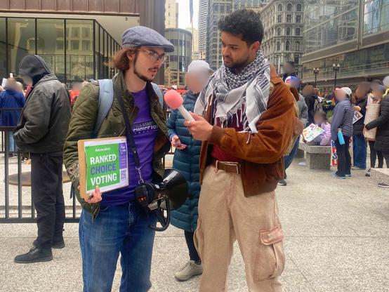 A FairVote Illinois volunteer holding a ranked choice voting sign while being interviewed by a street reporter