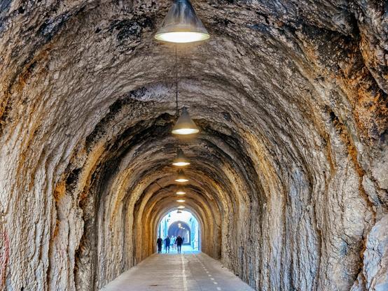 A tunnel with rock walls and a footpath and cycle way, leading towards the light