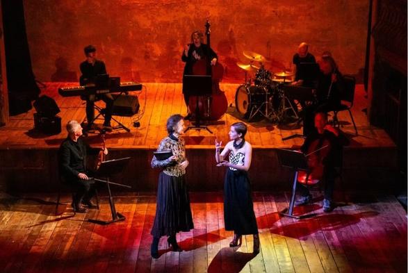 Two women on stage surrounded by musicians.