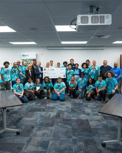 KC Current staff and players posing with BOA staff and students in the STEM lab. The players are holding a large check.