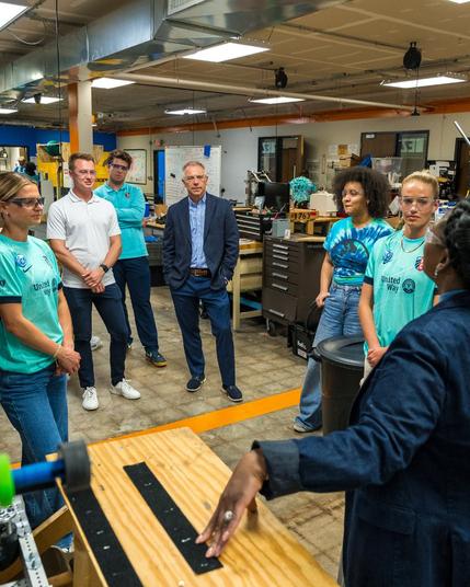 KC Current staff and players and BOA staff listening to a woman talking about items in the STEM lab.