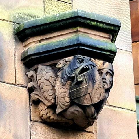 A sculpture of St George cowering behind his shield as a dragon bites into it.