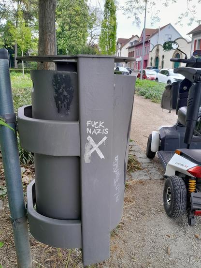 The scoot-chair is parked next to a trash can emblazoned with FUCK NAZIS, and the Shitter logo, which is a sans-serif swastika.
