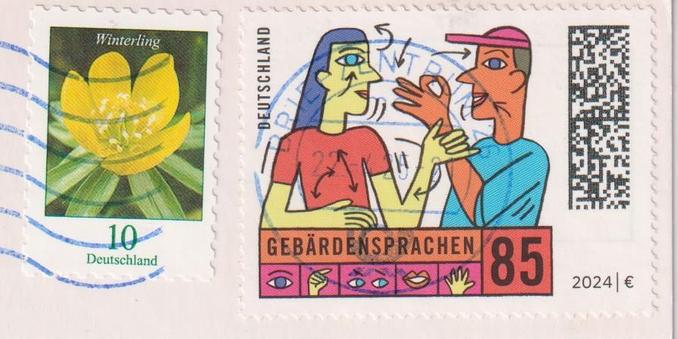 Stamps of a postcard from Germany.
One 10ct stamp with a yellow flower on it, a Winterling.
One 85ct stamp with two people talking to each other in sign language. It also has the word "Gebärdensprache" (sign language) with eyes and signs on it.
