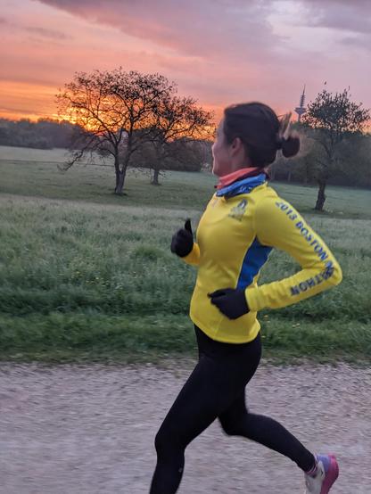 Katrin beim ersten Lauf der Challenge im Niddapark. Im Hintergrund ist der Frankfurter Europaturm und ein leuchtend roter Sonnenaufgang zu sehen.