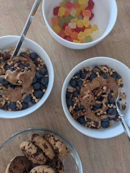 Unser zweites Frühstück: Zwei Schalen mit Milchreis und einem Topping aus Blaubeeren, Mandelmus und Pekannüssen, eine Schale mit Schokokeksen und eine Schale mit veganen Gummibärchen.