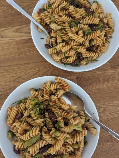 Unser Mittag- und Abendessen für Tag 1 der Challenge: Zwei weiße Teller mit veganem Nudelsalat stehen auf einer Tischplatte aus Holz.
