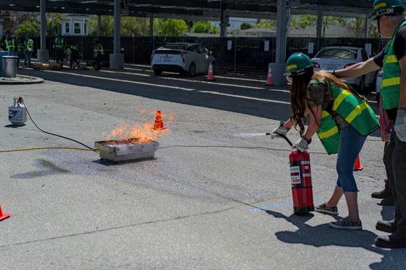 Two CERT members on the right practicing using a fire extinguisher to put out a simulated fire using a special device that uses propane to light a fire and some sensors to turn the fire off when you sweep water across the base