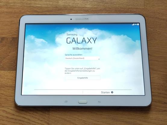 Foto des erwähnten Tablets. Es ist eingeschaltet und zeigt den Samung Galaxy Willkommensbildschirm, der zur Auswahl einer Sprache auffordert.