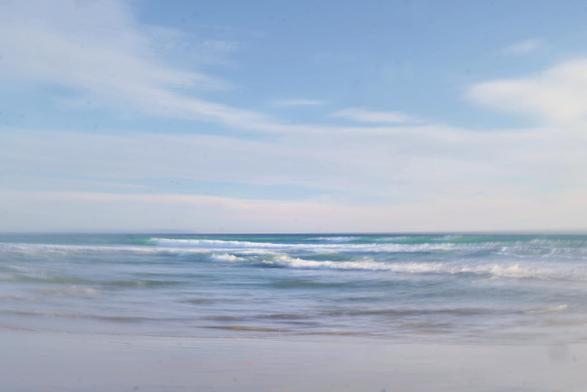 A blurry photo of a beach with the blue sea and small, breaking waves.