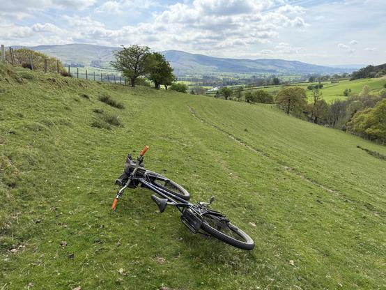 Bike laying on a fellside with a vague track running into the distance