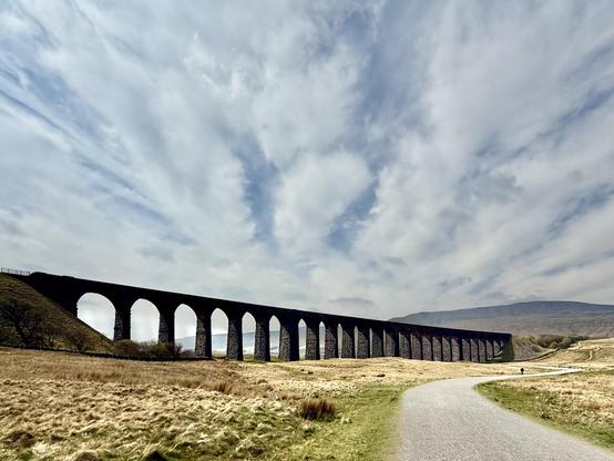 Viaduct under fluffy clouds with a track running towards it