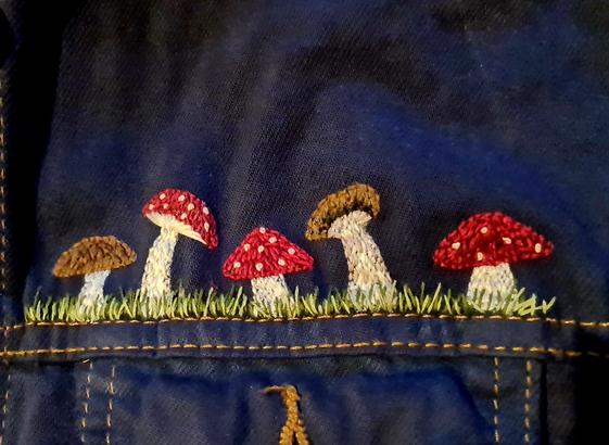 Handgearbeitete Stickereidetails auf einer Jeansjacke. Zu sehen sind 5 Pilze in Gras. Drei Fliegenpilze, ein Steinpilz und ein Austernseitling.
