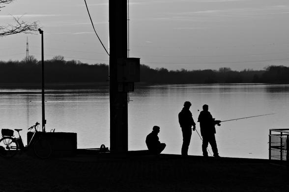 Black and white photo of shilouettes of people fishing in a river.