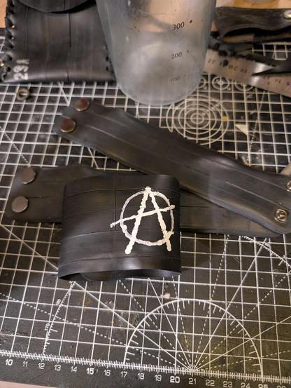 Photo of wristbands made from inner tube rubber with snap buttons, one of which has an Anarchist symbol.