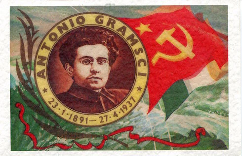 A drawing of Antonio Gramsci's face surrounded by the text 'Antonio Gramsci 23.1.1891 - 27.4.1937', on a background with a communist and Italian flag.