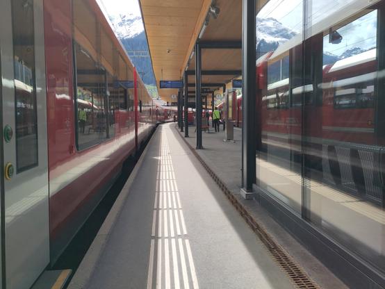 Foto. Zwei rote Züge und eine spiegelnde Glasscheibe im Bahnhof.