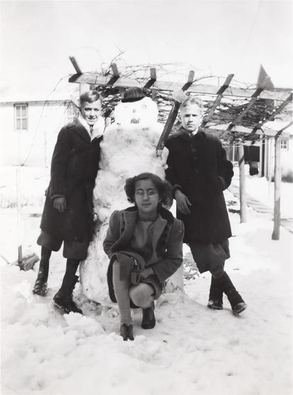 Three kids around a snowman (one to either side and one crouching in front) looking tough.