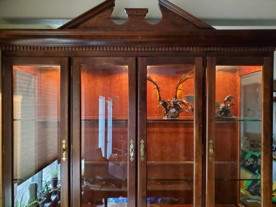 A beautiful hardwood glass-fronted cabinet with 4 doors. The cabinet is softly lit from above within. On the top shelf behind the center right door, a five-headed dragon "miniature" snarles out at you. With spread wings, it's nearly a foot tall and over a foot wide. The top shelf center left is bare, waiting for another impressive mini to be placed