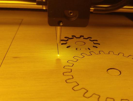 Picture of a lasercutter busy, with two gears already cut. Taken through the yellow cover