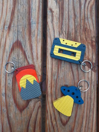 Porte-clés en lances à incendie et chambre à air de tracteur upcyclées :
- un OVNI bleu canard avec faisceau jaune
- un paysage avec montagnes kakies, soleil jaune et ciel orange et rouge
- une cassette audio bleue foncé et jaune