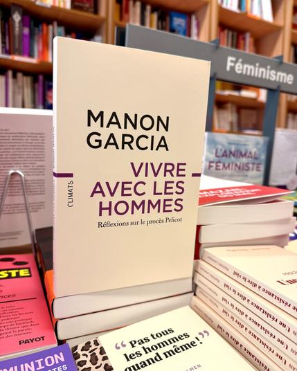 Livre Vivre avec les hommes au milieu d’une table de livres sur le Féminisme en librairie et à côté d’autres ouvrages sur les violences sexistes et le procès Mazan. La couverture est beige avec le titre écrit en mauve et le nom de l’autrice au-dessus en noir.